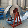 A large roll of silver metallic aluminum coil wound on a red metal support frame inside a factory workshop.